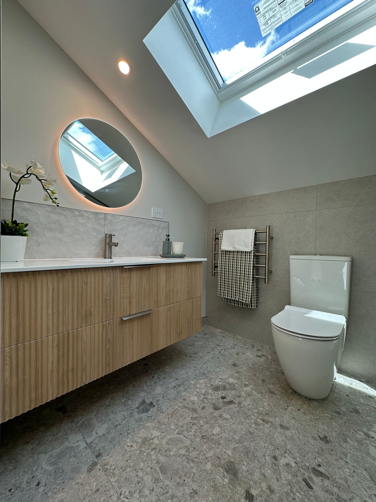 A Cromwell bathroom under a skylight: 600×600 porcelain on the walls, a terrazzo-look floor, and a textured ceramic splashback running the length of the vanity.