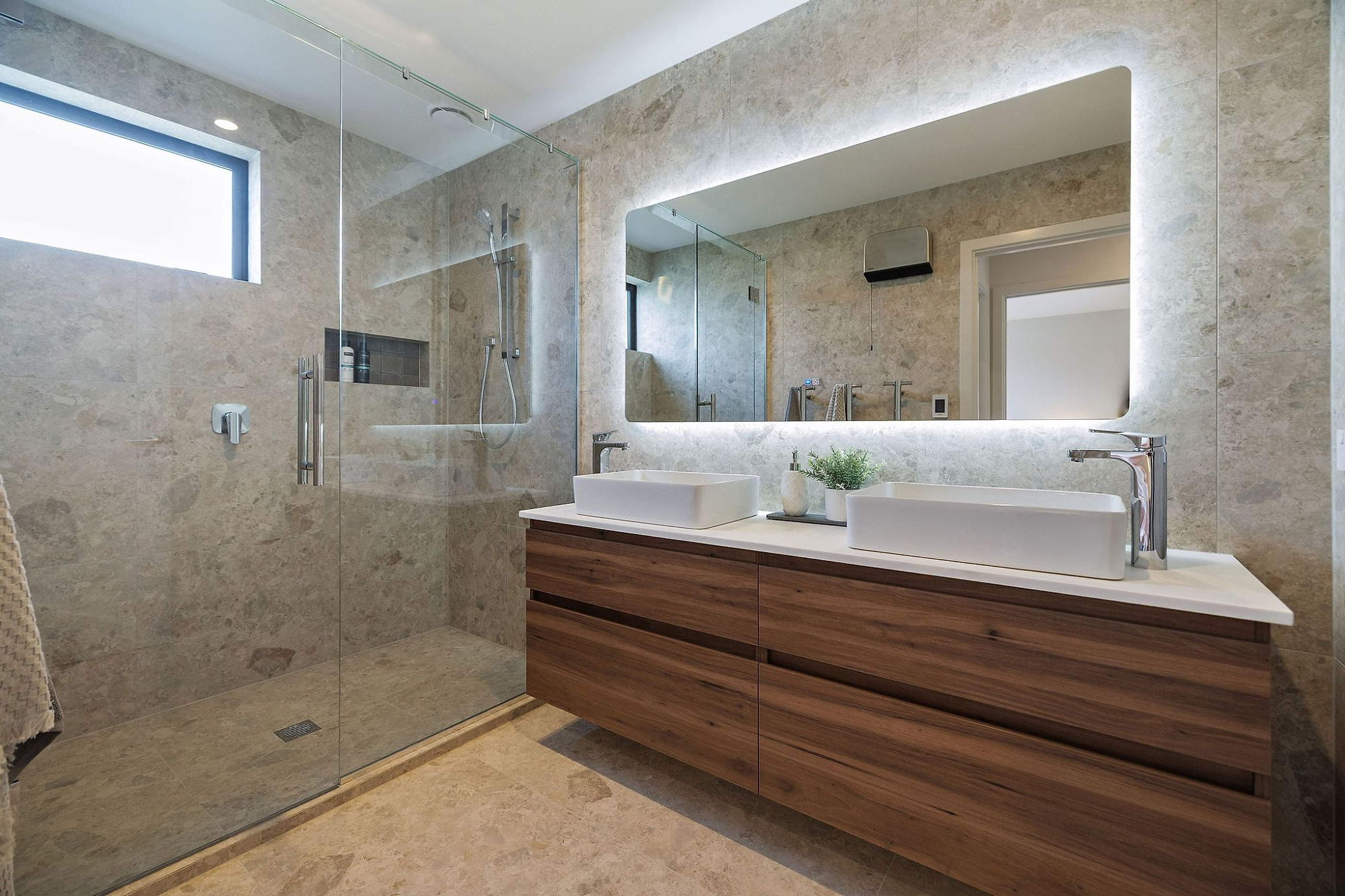 A finished bathroom: stone-look wall tile, a walk-in shower with no hob, and the floor running through from the room into the shower without a step.