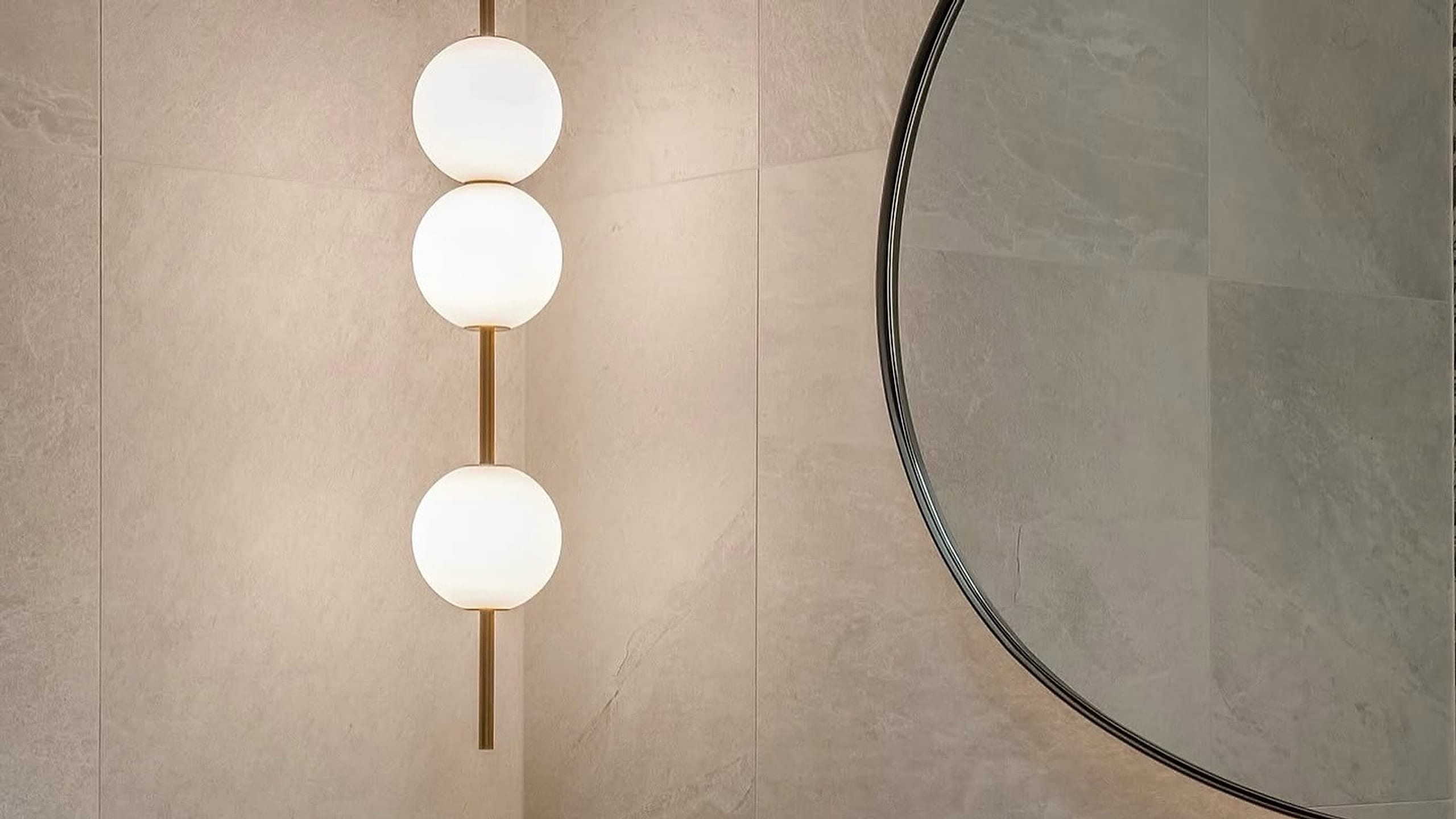 Large format stone-look porcelain panels on a bathroom wall, with the joints running unbroken behind a pendant light and an arched mirror.