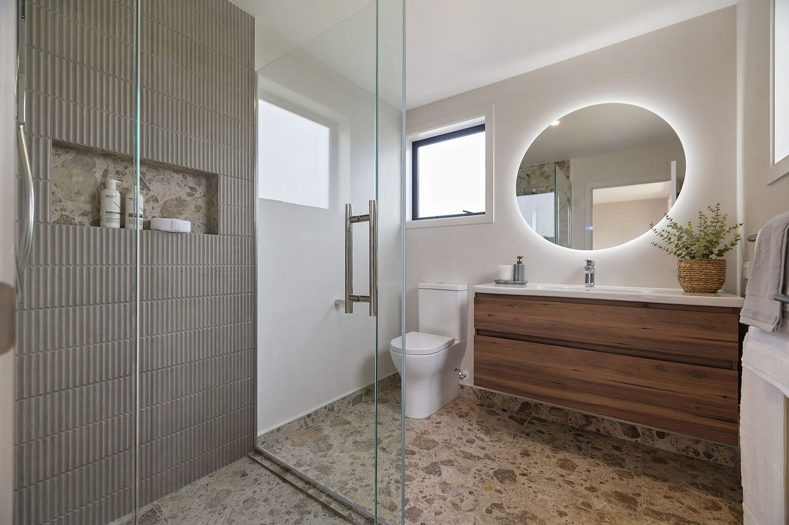 A walk-in shower finished in fluted vertical tile, with the floor material returned inside the niche and the shower floor running level with the room.